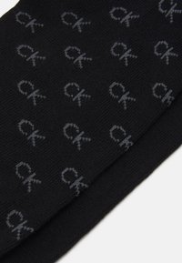 Sorte sokker med en myk tekstur, som har et gjentagende grått "ck" logo mønster. Designet er enkelt og ensartet over stoffet.