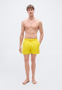 Κίτρινα μαγιό σορτς από ελαφρύ υλικό, με ελαστική μέση και κορδόνι, πλαϊνές τσέπες και διακοσμητικό λογότυπο.