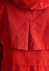 Czerwony materiał z detaliczną, złożoną zakładką i szwem, prawdopodobnie tył ubrania z kapturem.