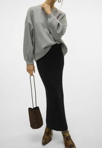 Sudadera gris de gran tamaño con hombros caídos, combinada con una larga falda de punto negra. Presenta un bolso de ante marrón y botas de tobillo con un diseño estampado.