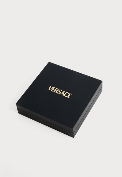 Boîte carrée noire avec logo VERSACE doré centré sur le couvercle, fermée et placée sur un fond blanc.