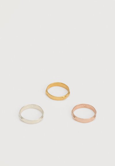 Tres anillos de metal liso en oro, plata y oro rosa, dispuestos en un triángulo sobre un fondo blanco.