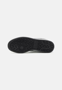 Black rubber sneaker sole with a textured tread pattern, featuring a white midsole and green accents along the upper edge.