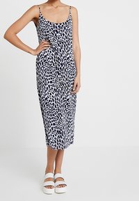 Granatowa i biała bezrękawnikowa sukienka midi w abstrakcyjny wzór, z cienkimi ramiączkami i luźnym krojem, w połączeniu z białymi sandałami na platformie.