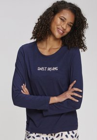 Navy long-sleeve shirt featuring "SWEET DREAMS" text in a light color, round neckline, and a soft, smooth texture. Paired with patterned pants.