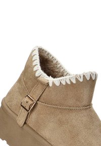 Botas de tobillo de ante marrón claro con un acabado texturizado, costuras decorativas en blanco en el cuello y un detalle de hebilla lateral para el ajuste.