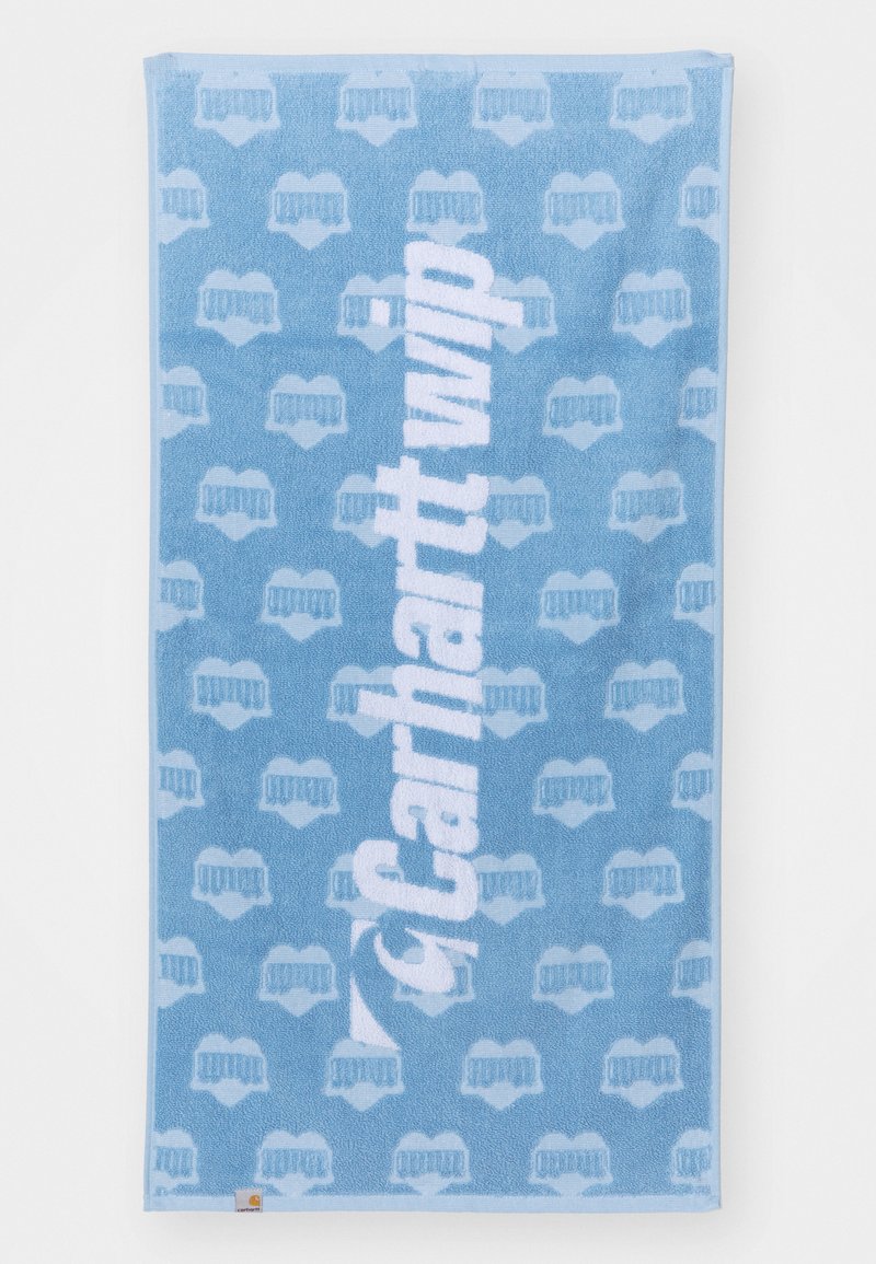 Light blue towel with textured feel, featuring repeated light blue pattern and large white "Carhartt WIP" logo in the center.