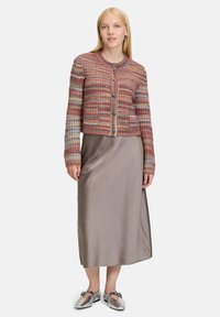 Woman wearing a multicolored knit cardigan, taupe satin midi skirt, and metallic silver flat shoes, standing against a plain background.