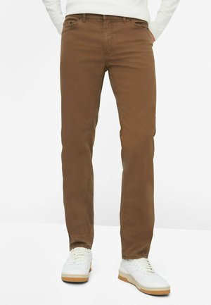Brune bomuldsbukser med lige ben-design, med sidelommer og lynlås, parret med hvide sneakers.
