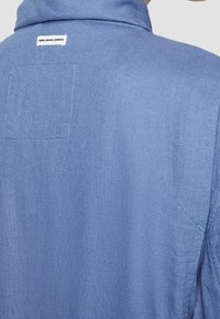 Jasnoniebieska kurtka dżinsowa z kołnierzem, tylną kieszenią naszywaną oraz widocznymi detalami szwów. Metka marki "Pepe Jeans London" na karku.