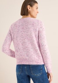 Jasnoróżowy sweter o marmurkowej teksturze, okrągłym dekolcie oraz ściagaczach przy mankietach i u dołu. Połączony z niebieskimi dżinsami.