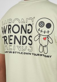 Světle zelené bavlněné tričko s výrazným černým textem: "ŠPATNÍ PŘÁTELÉ" a kreslenou postavičkou se zašitým úsměvem a červeným srdíčkem.