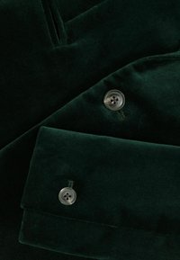 Tissu en velours vert foncé avec un détail de bouton et un éclat subtil, au design ajusté et à la texture lisse.