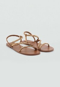 Sandali piatti marroni con cinturini intrecciati dorati, caratterizzati da un design semplice e una suola liscia, adatti per un uso casual.