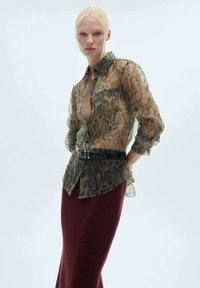 Blusa trasparente con motivo a serpente, colletto, chiusura a bottoni e maniche a tre quarti, abbinata a una gonna lavorata in bordeaux e una cintura nera.