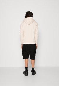Felpa rosa chiaro con cappuccio, abbinata a pantaloni cargo neri con tasche laterali, indossata con calzini neri e sneaker.