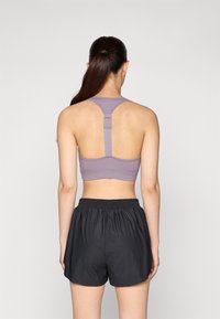 Violet sportinis liemenukas su sportiniu nugaros dizainu, turintis reguliuojamus dirželiais ir horizontaliu siūlu; derinamas su juodomis elastinėmis juosmens šortais.