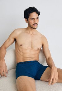 Boxer da uomo blu con elastico nero con la scritta "BJÖRN BORG". Tessuto liscio, design aderente e lunghezza della gamba corta.