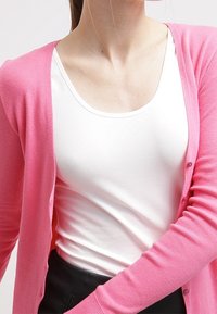 Pink knitted cardigan with a smooth texture, featuring buttons and a V-neck, layered over a plain white top.