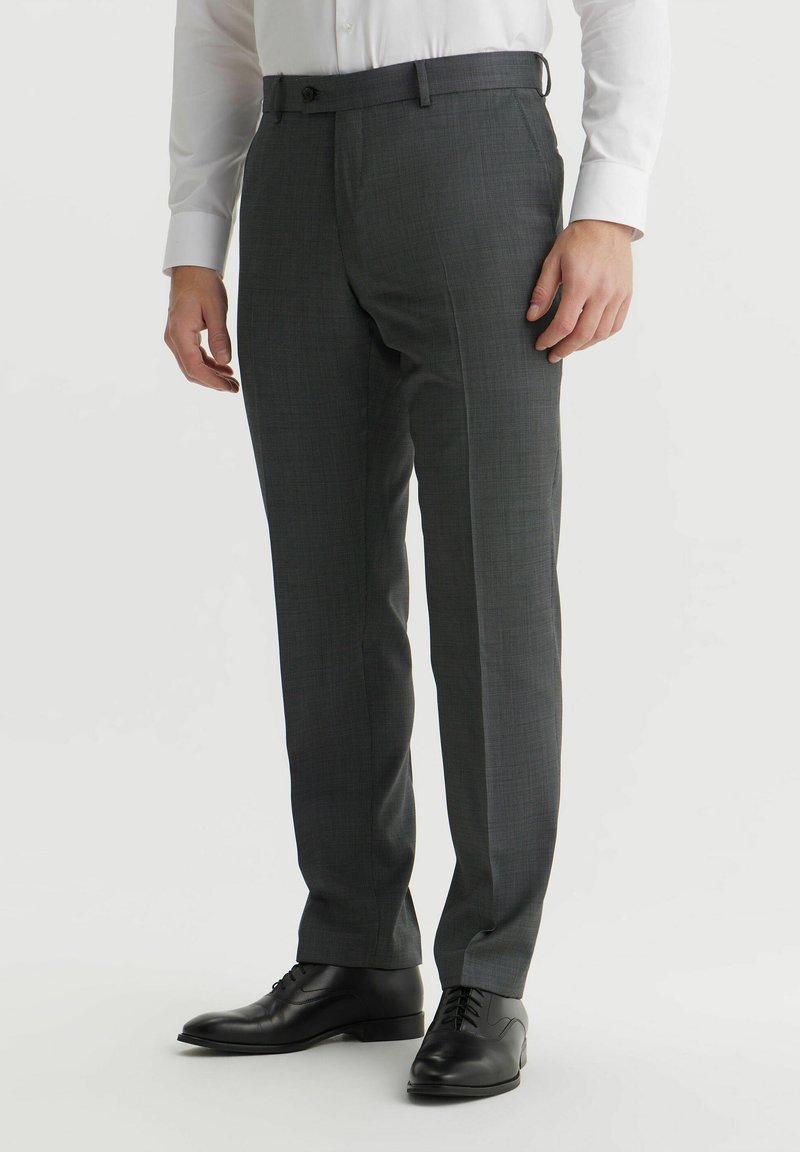 Szare spodnie w deseń o dopasowanym kroju, z paskami na pasek, pojedynczym guzikiem z przodu, zestawione z czarnymi skórzanymi butami.