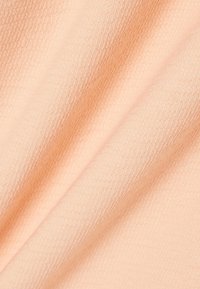 Tissu doux de couleur pêche avec un motif tricoté fin et texturé et des plis ombrés subtils.