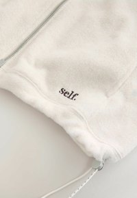 Weißer Fleece-Reißverschlussjacke mit strukturierten Oberfläche. "self."-Logo in Braun an der Hemmung gestickt. Mit Zugkordel und metallischen Details.