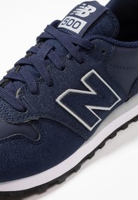 Námořnické tenisky New Balance 500 s texturovanou semišovou a syntetickou svrchní částí, šedými akcenty, kulatými tkaničkami a vzorovanou gumovou podešví.