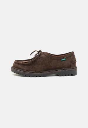Chaussure montante en daim marron pour homme avec semelle noire épaisse à crampons et petite étiquette verte "Polo" sur le côté.