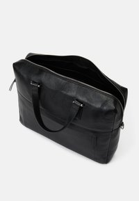 Crna kožna torba za laptop s teksturiranim finišem, gornjim zatvaračem, dvostrukim ručkama i prostranim unutarnjim dijelom. Ima suptilno šivanje i minimalistički dizajn.