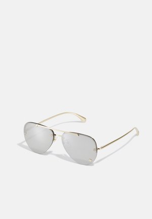 Lunettes de soleil teintées de gris avec une monture en métal doré, de forme angulaire et avec des plaquettes de nez proéminentes. Présente de petits accents dorés sur la monture.