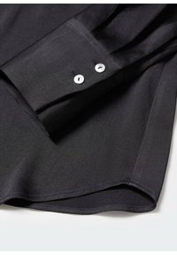 Poignet de chemise à manches longues noire avec deux boutons blancs et couture détaillée sur un fond clair.