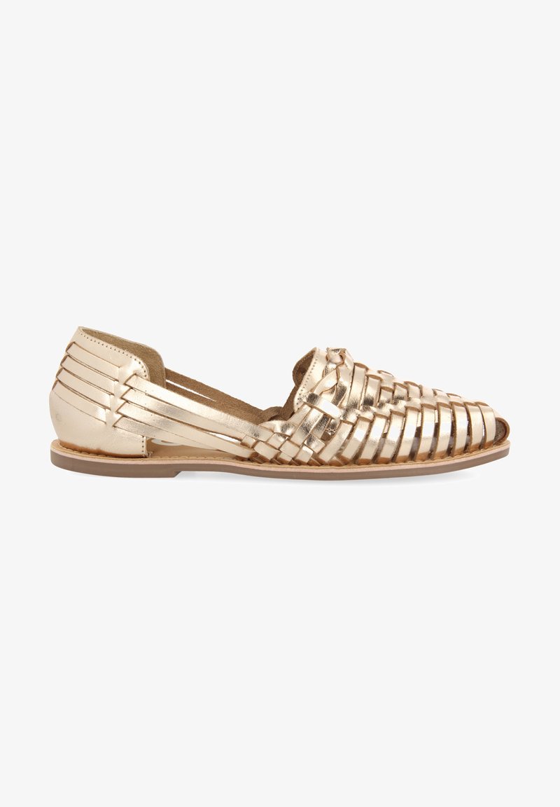 Des chaussures plates en or métallique présentent un design tissé, des côtés ouverts et une semelle plate. La tige a une texture lisse avec une légère brillance.