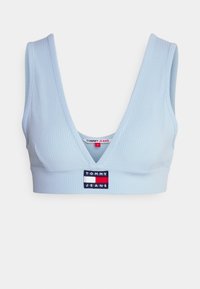 Světle modrá žebrovaná braletka s hlubokým výstřihem do V; na přední straně je umístěna nášivka Tommy Jeans v červené, bílé a modré barvě. Hladká textura.