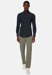 Námořnická košile s dlouhým rukávem, jednobarevná, klasický límeček, přiléhavý střih; kombinována se světle šedými kalhotami a bílými teniskami.