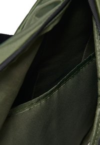Κοντινή λήψη σκοτεινού πράσινου υφασμάτινου τσεπίου μέσα σε τσάντα με ορατές ραφές και μέρος ενός ανοικτού φερμουάρ.