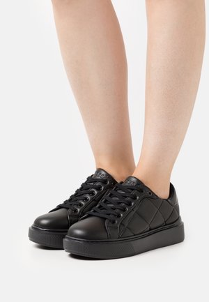 Sneaker in pelle nera trapuntata con lacci piatti e suola in gomma testurizzata, caratterizzate da un logo discreto sulla linguetta.