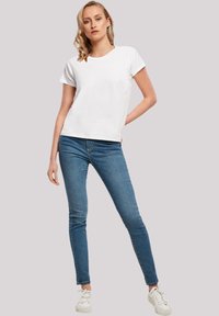 White short-sleeve t-shirt with a round neckline, paired with slim-fitting blue jeans and white sneakers, set against a neutral background.