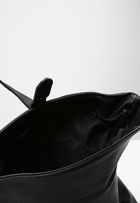 Černá kožená taška přes rameno, otevřený vrch s texturovaným povrchem, vnitřní látková podšívka odhaluje prostornou přihrádku a detail s kapsou na zip.