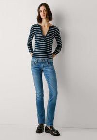 Haut à rayures bleu marine et blanches à manches longues avec un décolleté en V et des détails de boutons, associé à un jean droit bleu clair et des mocassins noirs.