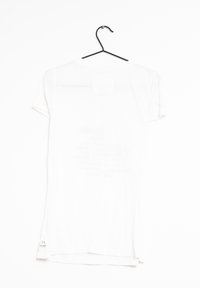 Camiseta blanca exhibida en una percha negra, con un cuello redondo, mangas cortas y un detalle de texto mínimo cerca del dobladillo.