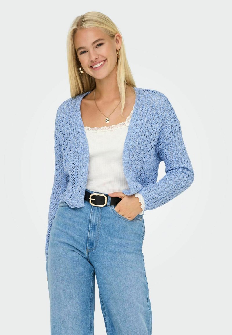 Cardigan a maglia blu chiaro con un motivo texturizzato, maniche lunghe e una vestibilità corta, abbinato a una maglietta bianca e jeans blu a vita alta.