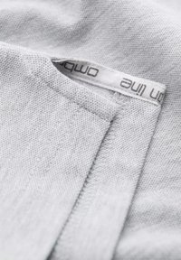 Ljust grått tyg med en texturerad väv, med en sydd etikett med varumärket. Kanterna är snyggt avslutade, utan fransar.