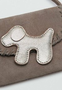 Portafoglio in suede marrone con un elemento decorativo a forma di cane in metallo argentato e dettagli cuciti. Texture liscia e design minimalista.