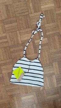 White and black striped fabric bag with a halter top design, featuring a keyhole cutout and knotted straps. Includes a brand tag.
