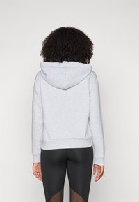 Grijze hoodie met een casual ontwerp, zachte textuur, en geribbelde boorden en onderkant. Draagt met zwarte leggings, wat een cropped pasvorm laat zien.