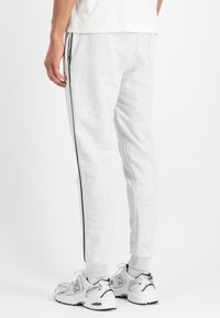 Svetlo sivi trenirka iz mehkega blaga, opremljena s črnimi stranskimi trakovi in ribastimi manšeti. Nosi se z belimi športnimi čevlji.