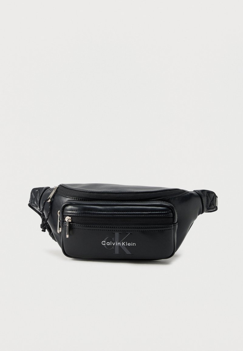 Μαύρο δερμάτινο τσαντάκι μέσης Calvin Klein με δύο θήκες με φερμουάρ και ρυθμιζόμενο λουράκι σε ανοιχτό φόντο.