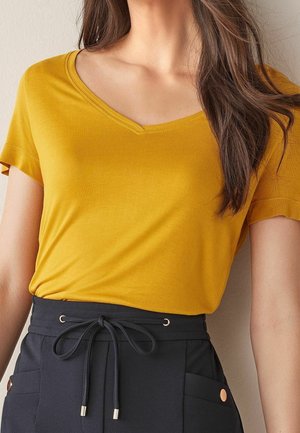 V-neck yellow t-shirt with short sleeves, made of soft fabric. Paired with navy trousers featuring a drawstring and metallic accents.