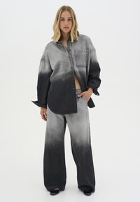 Completo in denim composto da una camicia con bottoni e pantaloni a gamba larga. Design a gradiente grigio con una texture morbida e una tasca sul petto della camicia.