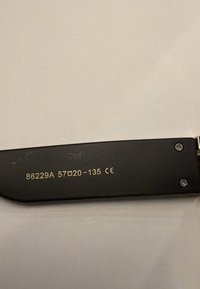 Schwarzer Bügel einer Brille mit goldfarbenem Text, der Modellnummer, Größe und CE-Zertifizierungszeichen auf einer hellen Oberfläche anzeigt.